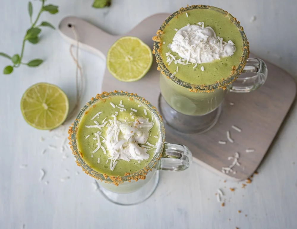An overhead view of two key lime pie smoothies topped with a dollop of coconut whip and shredded coconut in glasses that have graham crackers on the rims.