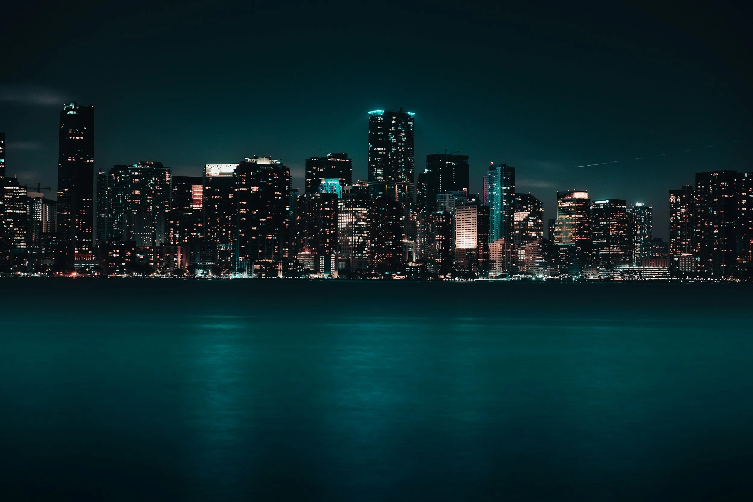 Night view of a city skyline with illuminated skyscrapers, seen from across a body of water in Miami, Florida.