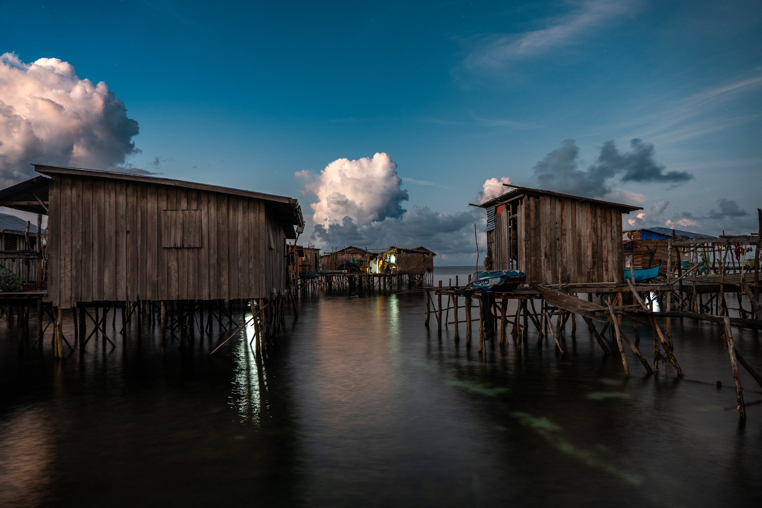 Stilt houses made of wood along a calm body of water under a partly cloudy sky during twilight.