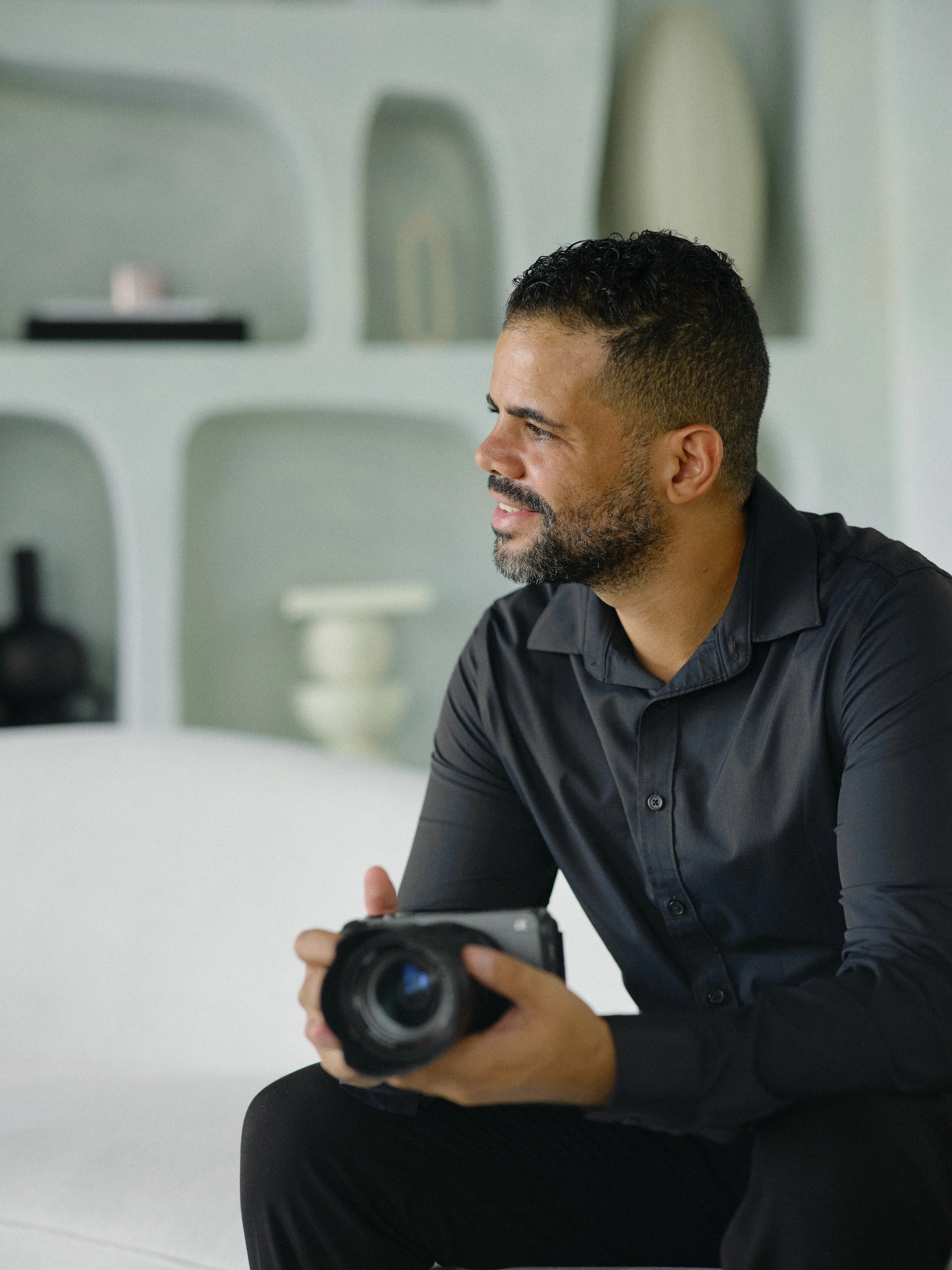 Man sitting on a white couch holding a camera, looking to the right.
