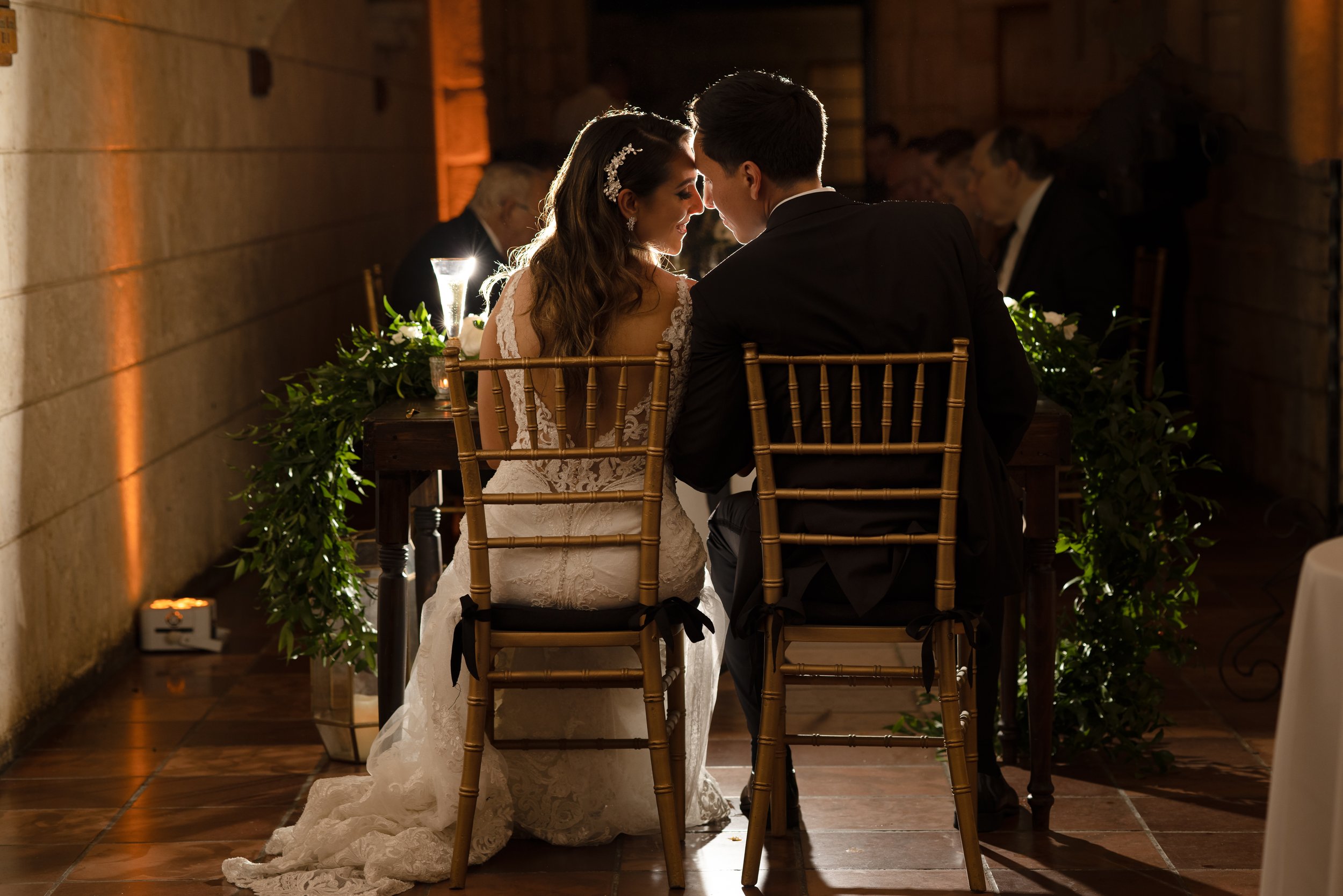 Bride and groom in wedding attire sitting face to face at a table during their wedding reception.