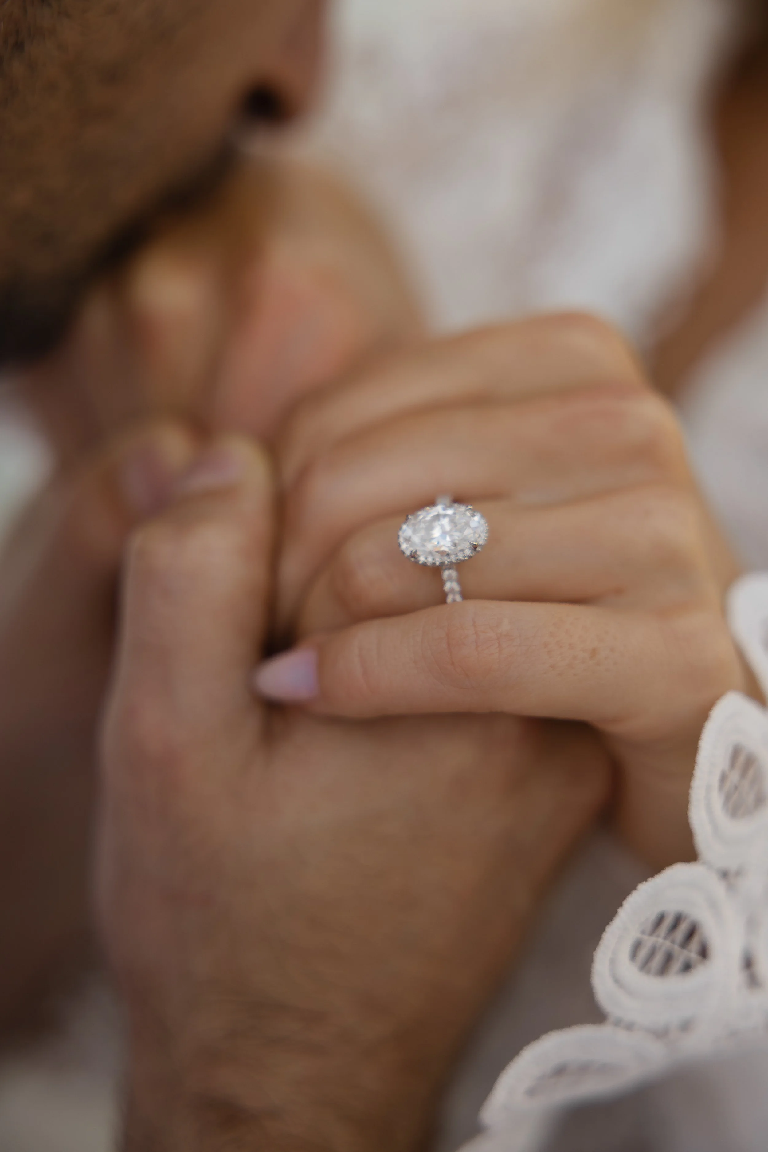 A man and woman holding hands, with the woman displaying a large diamond engagement ring.