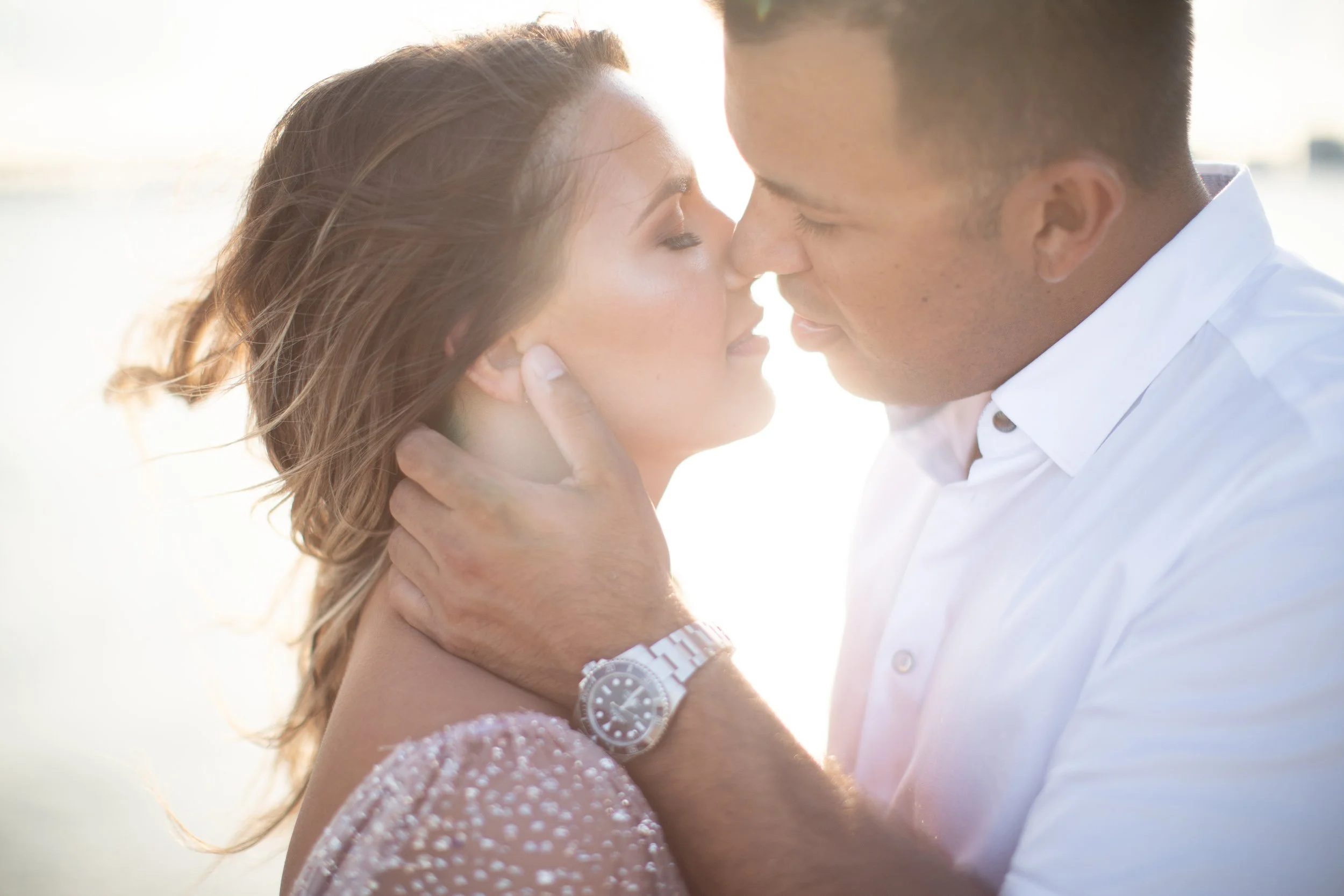 A man and woman intimately close, touching foreheads with eyes closed, with bright sunlight in the background revealing a romantic moment.