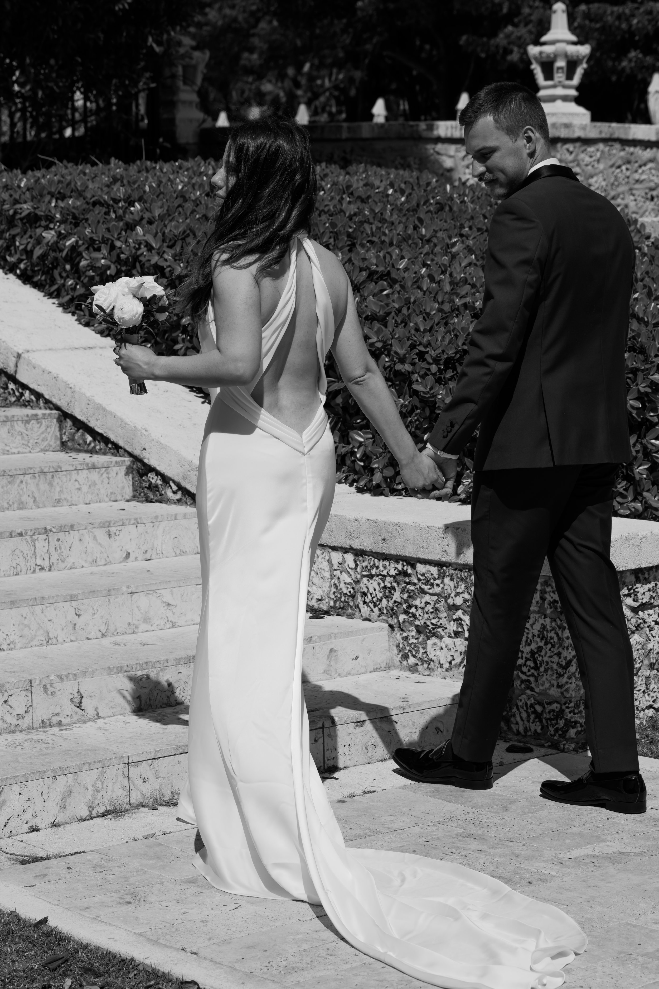 A bride and groom holding hands during a wedding ceremony outside, with the bride holding a bouquet of flowers.