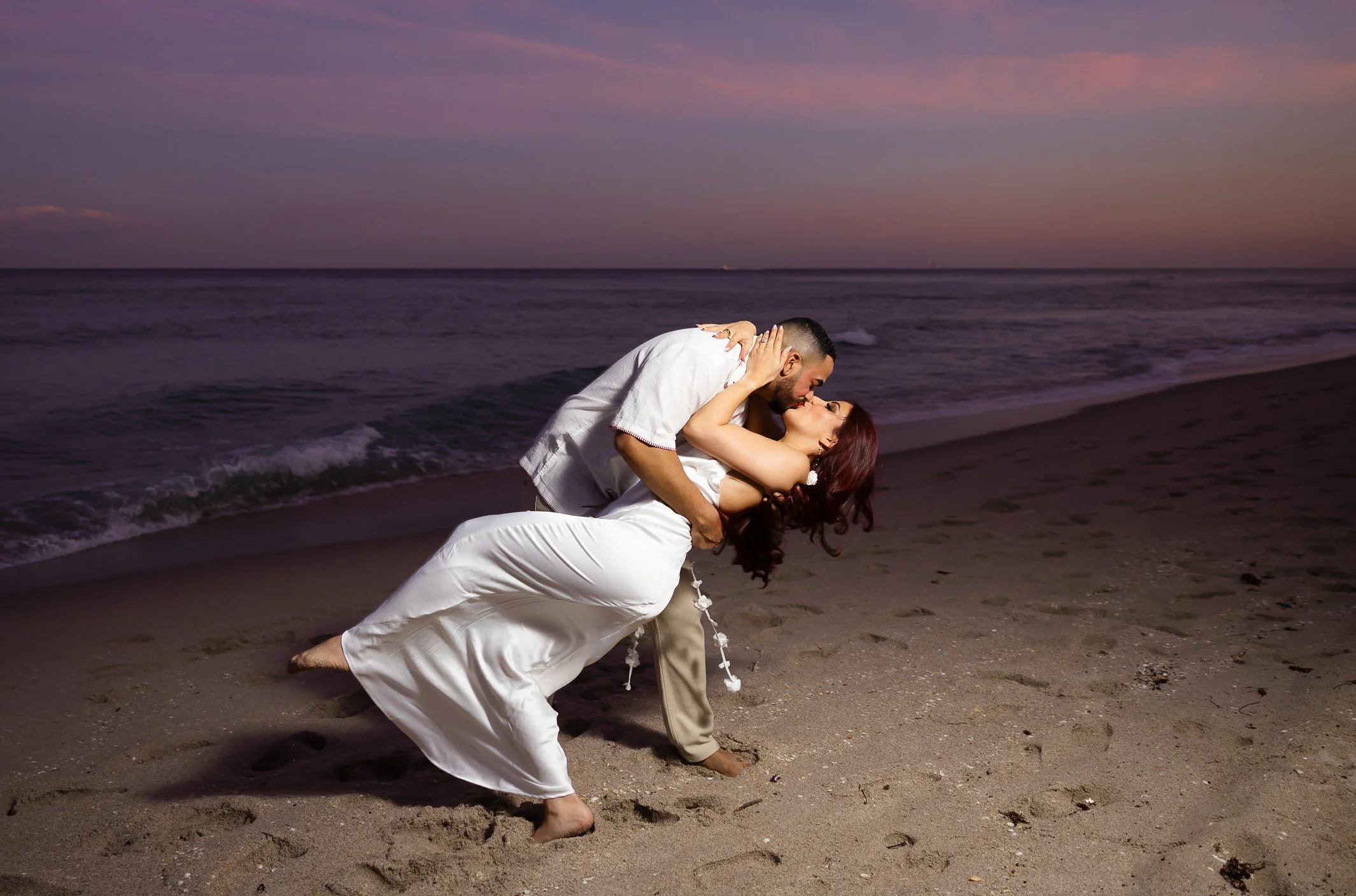 A couple on the beach at sunset, sharing a romantic kiss with the man dipping the woman.