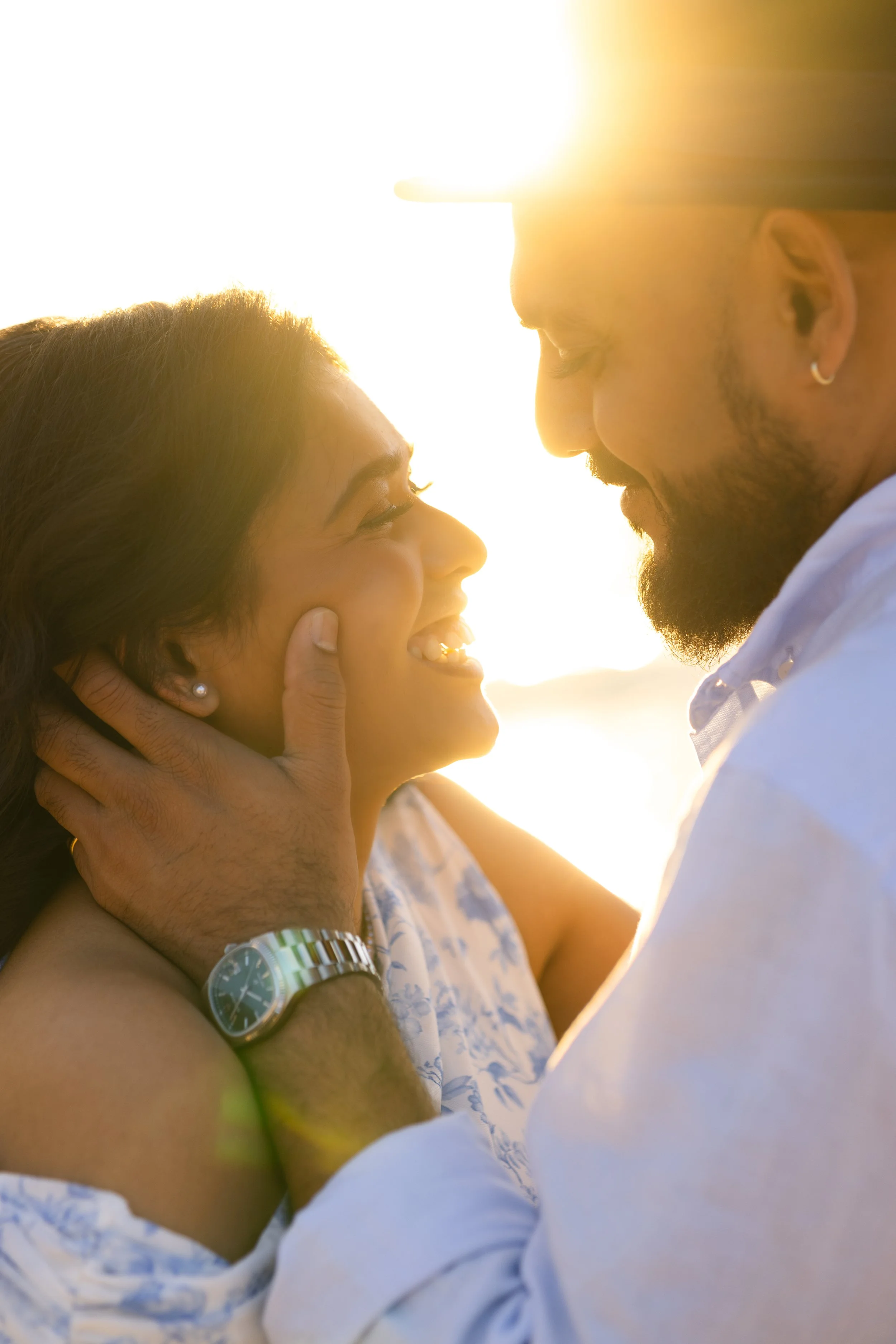 A couple smiling and looking into each other's eyes with sunlight in the background.