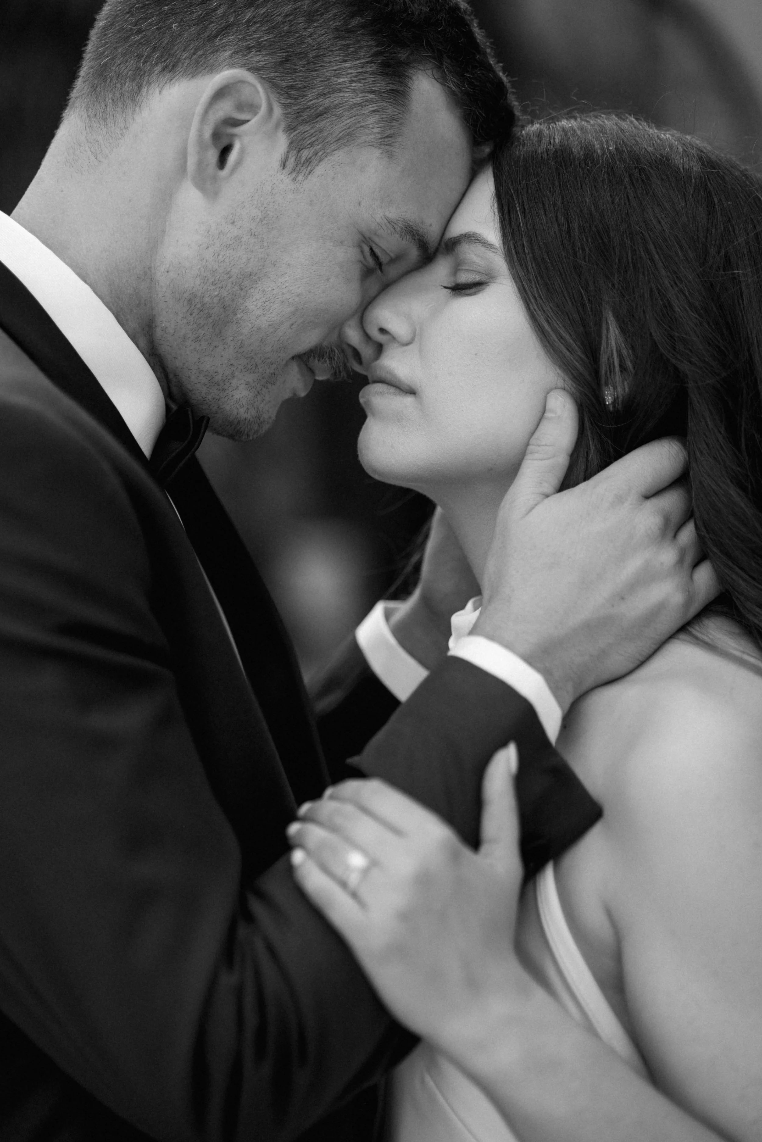 A black and white photo of a couple in an intimate moment with foreheads touching, one man gently holding the woman's face.