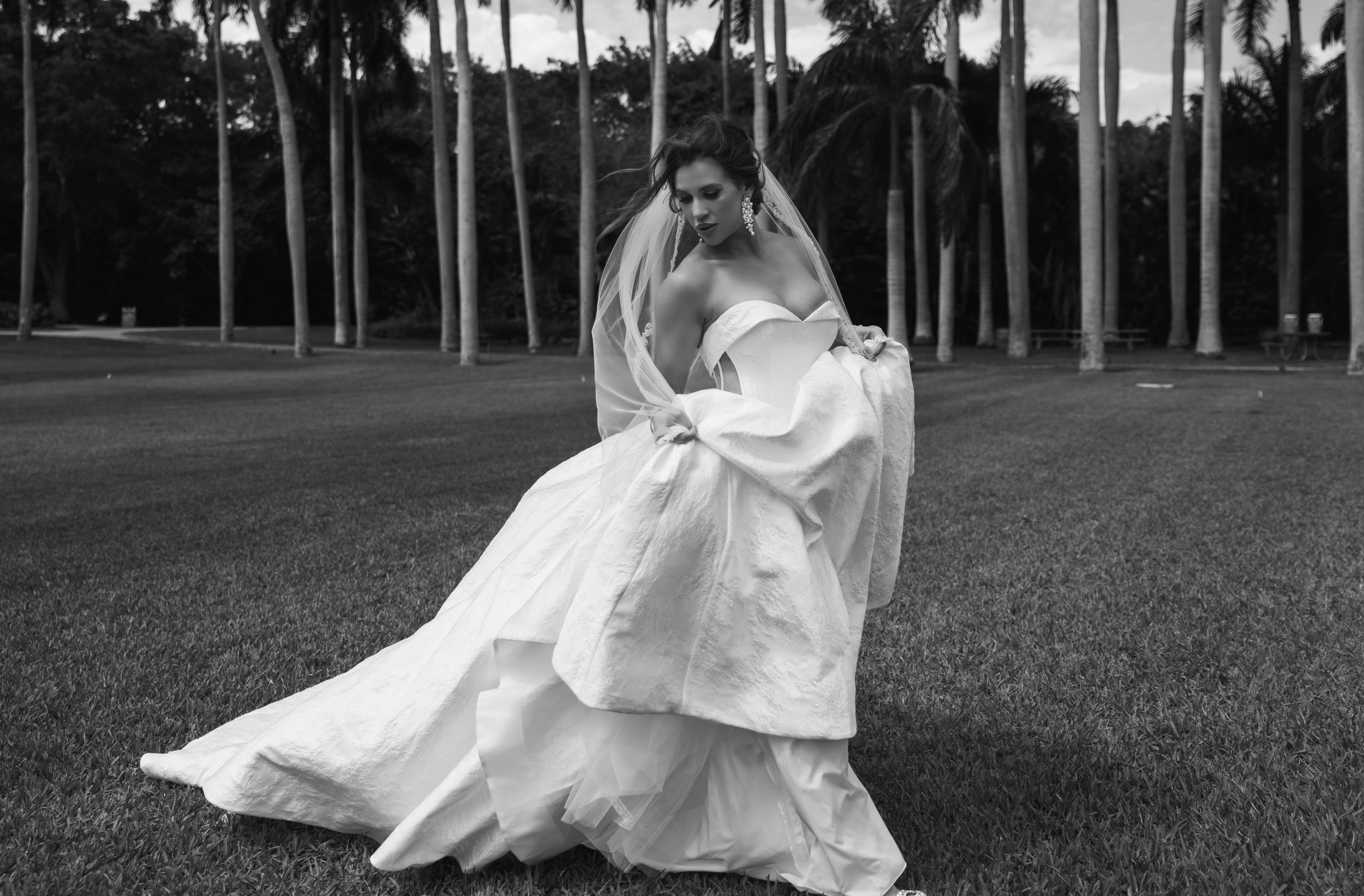 A bride in a strapless wedding dress standing on grass with trees in the background.
