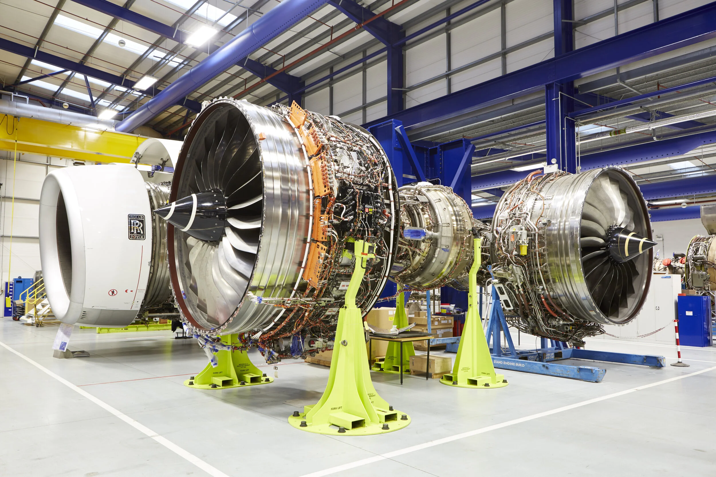 Large aircraft jet engines with detailed internal components and wiring on assembly stand inside a manufacturing facility.