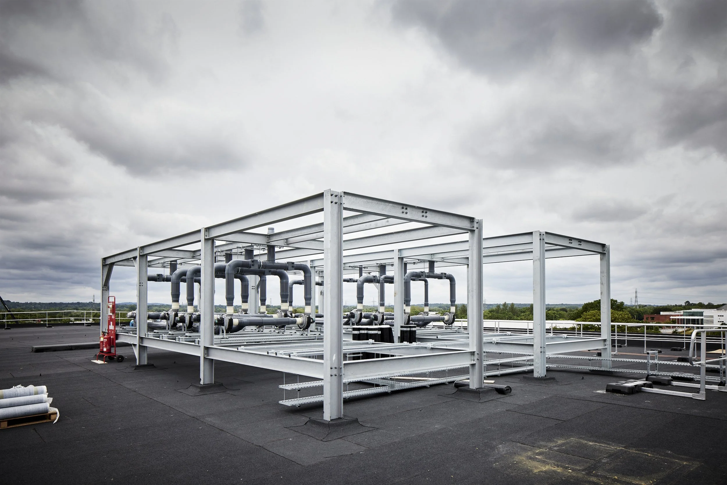 Rooftop heating, ventilation, and air conditioning (HVAC) system with interconnected pipes and metal framework under cloudy sky.