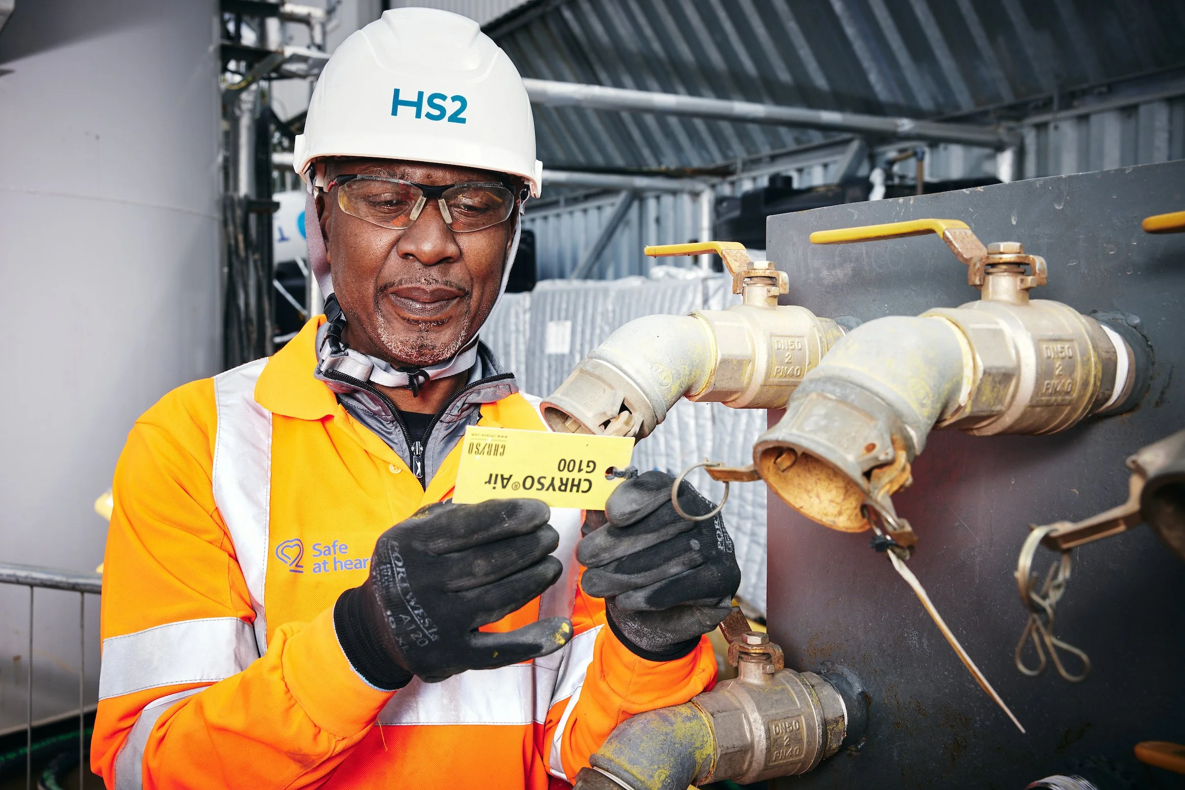 A worker in safety gear inspecting pipes with a yellow tag in an industrial setting.