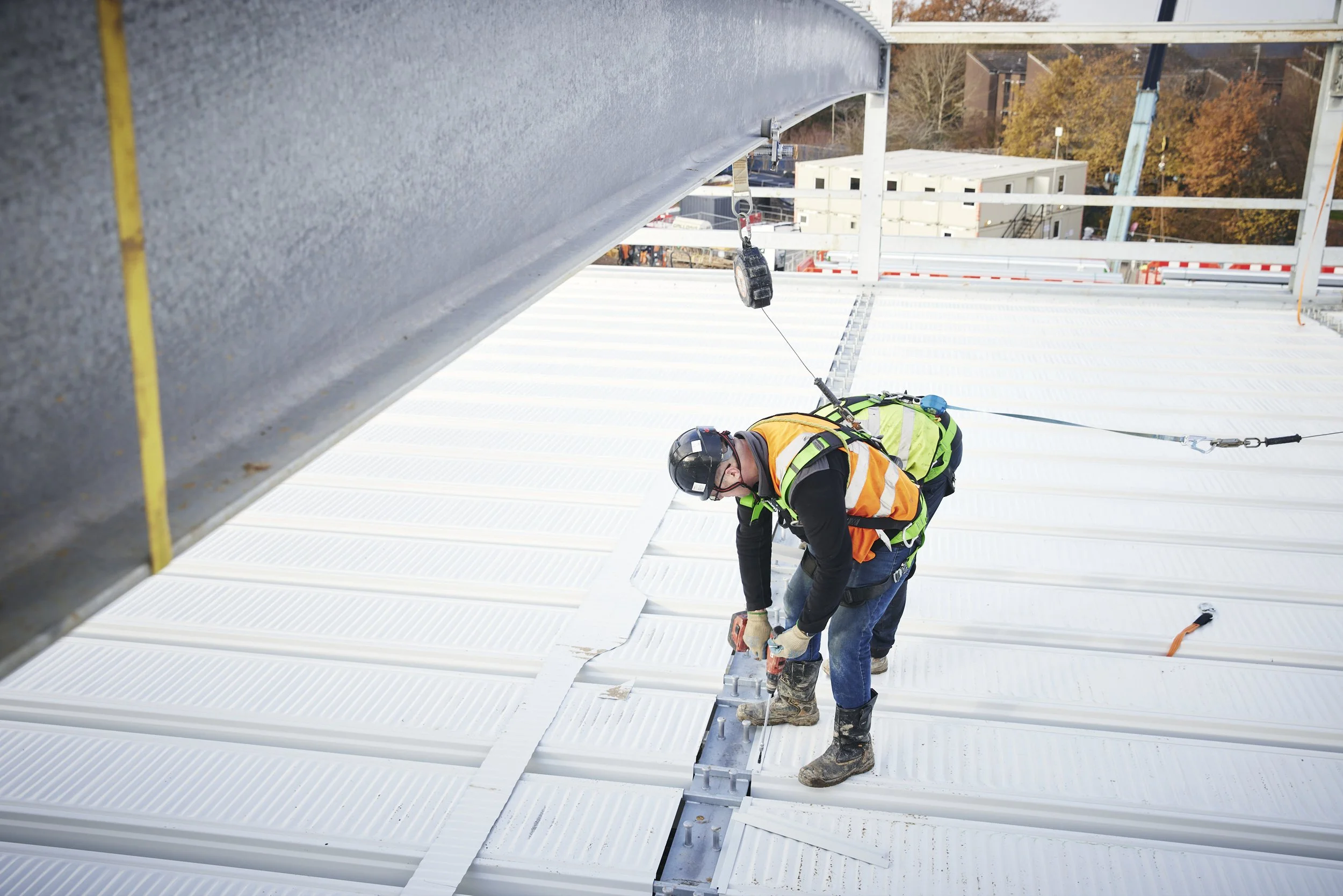 Worker with safety harness and helmet installing or repairing roofing on a commercial building