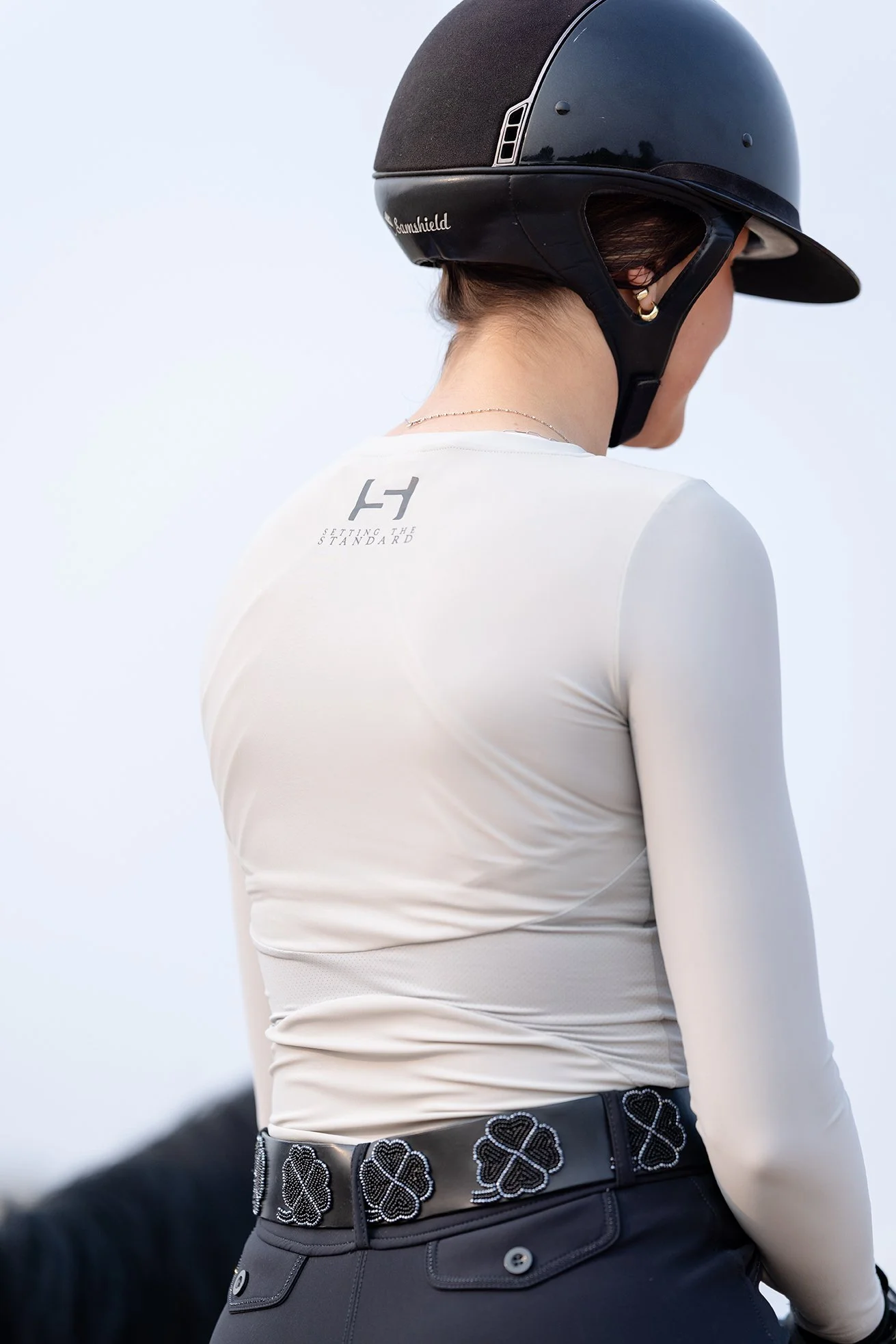 Back view of rider in grey STS Equestrian shirt and Samshield helmet showing "Setting the Standard" logo.