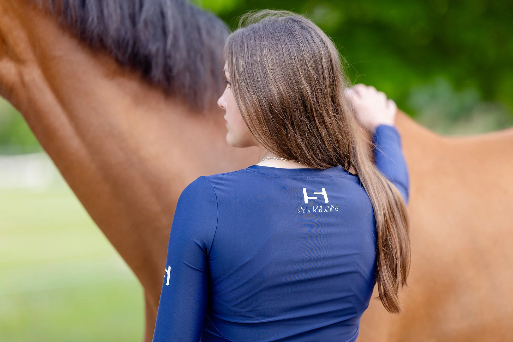 Back view of rider in navy STS Equestrian shirt petting her horse.