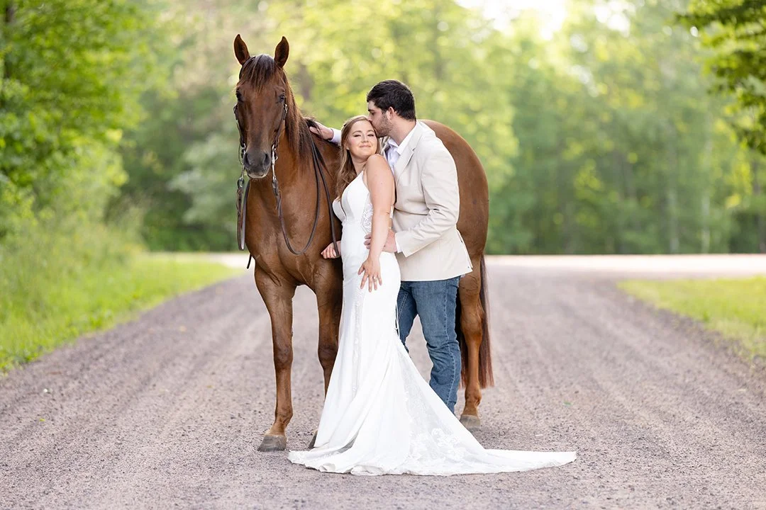 Couple sharing a romantic moment beside their chestnut horse during an equestrian bridal portrait session on a quiet country road in Wisconsin.