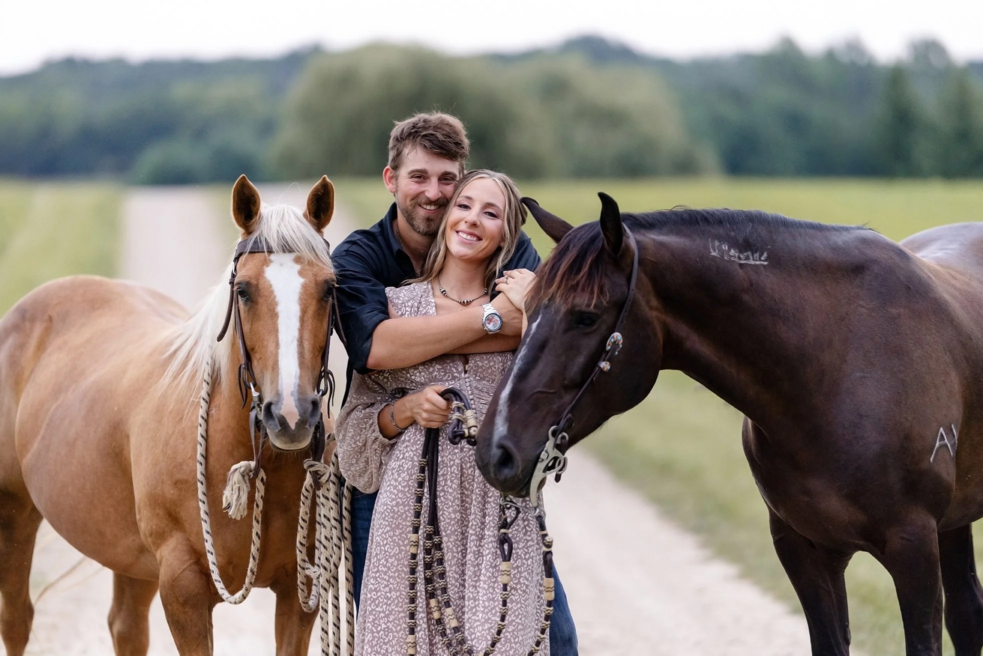 Amber and Isaac stand embraced between their horses, Ellie and Atlas, creating a warm and connected portrait during their western equestrian engagement session in rural Wisconsin.