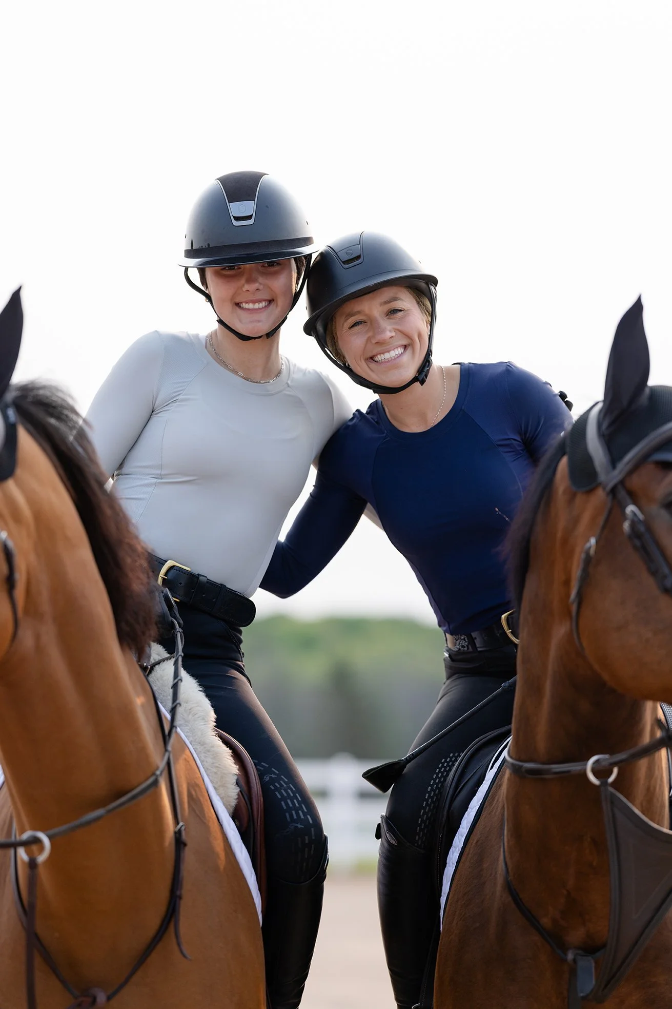 Two smiling equestrians in STS shirts posing while mounted on their horses.
