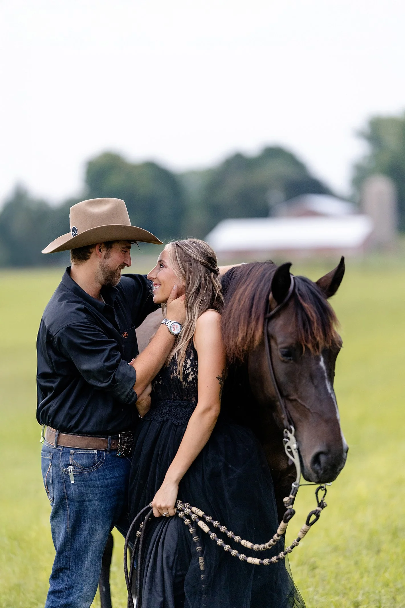 Amber and Isaac share a soft moment beside her mustang Atlas during their western equestrian engagement session in Poynette, Wisconsin, with rolling farm fields in the background.