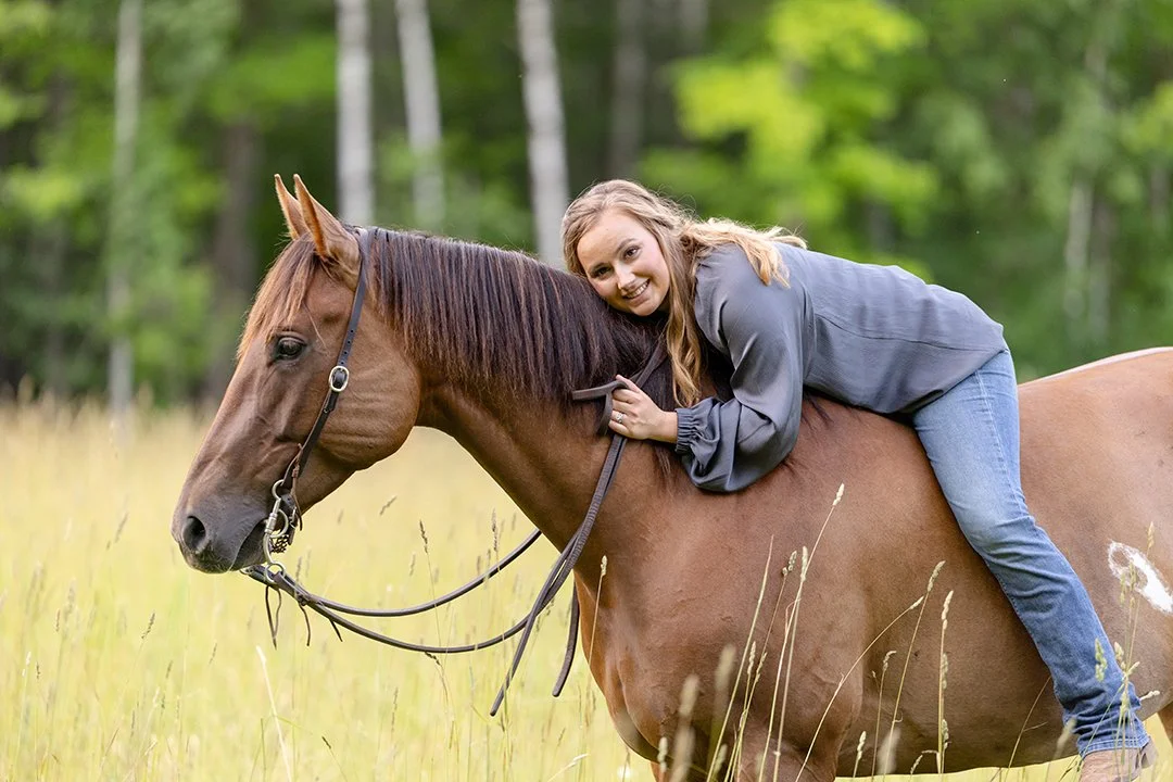 Woman laying across the back of her chestnut horse during a relaxed horse and rider portrait session in a grassy Wisconsin field.