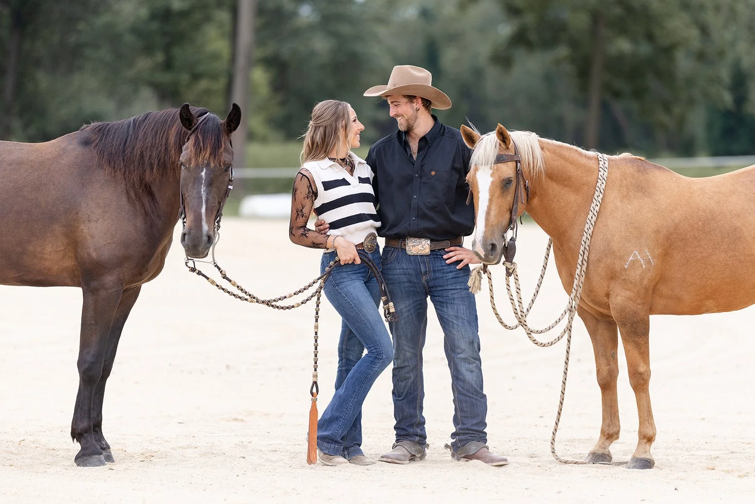 Amber and Isaac stand together holding their horses, Atlas and Ellie, during their equestrian engagement session at Advanced Horsemanship in Poynette, Wisconsin. Both horses frame the couple beautifully in the arena.