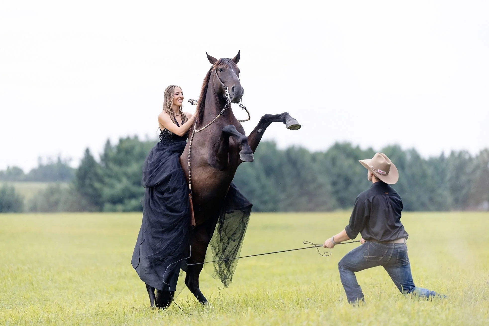 Amber rides her mustang Atlas as he rears in a field while Isaac cues him from the ground, creating a powerful and cinematic moment during their equestrian engagement session in Wisconsin.