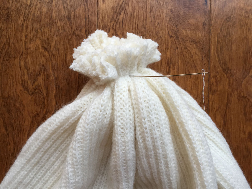 STEP 3: Flip the sweater tube inside out. Sew a half inch basting stitch around the entire bottom edge of the sweater. Pull tight and secure with a few additional stitches.