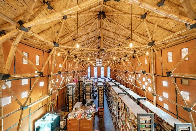 The simple form of the structure as seen from the outside is contrasted by the complex web-like structural trusses seen in the interiors. The earth and bamboo library has a double height space which regulates natural lighting and air quality through the fenestrations. The walls bear a natural palette of pastel yellows and reds of the local clay varieties used in plasters. The ceiling is finished with bamboo mats not only for aesthetic but also for its insulation properties.