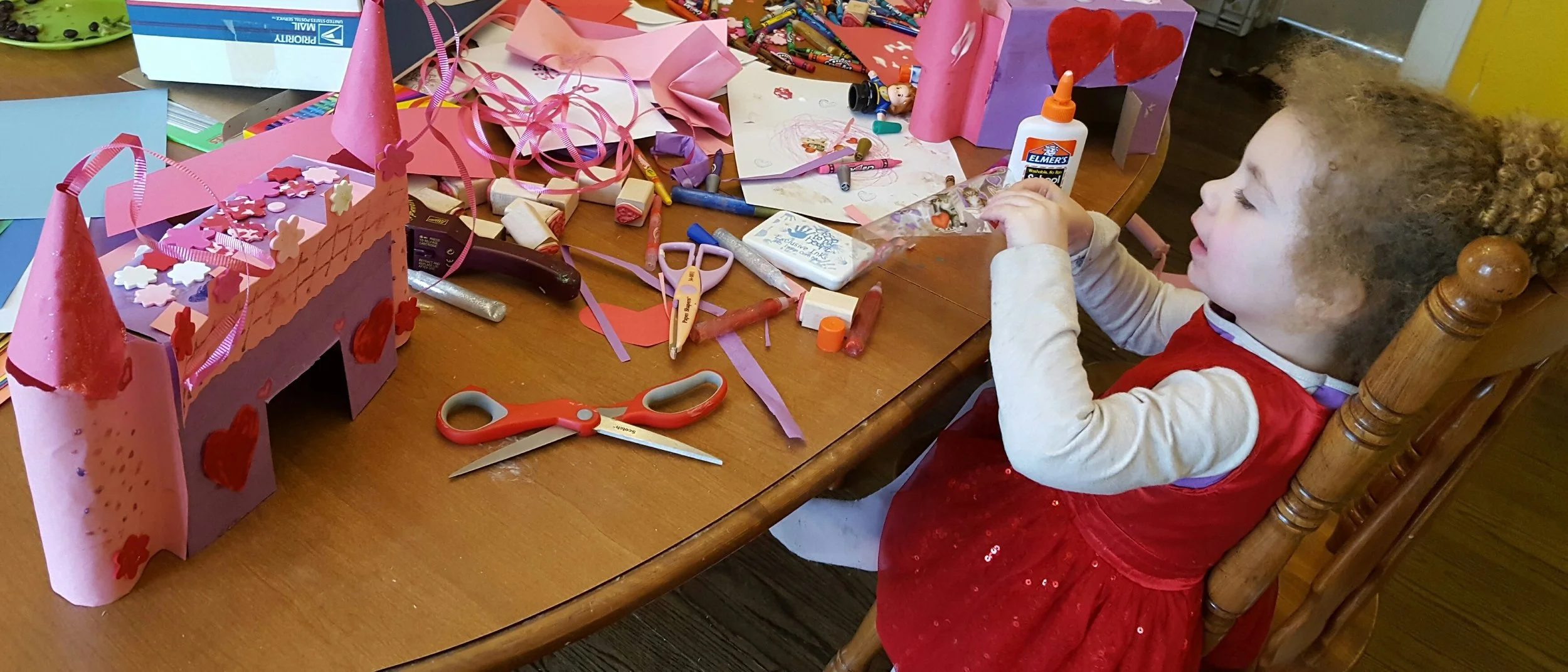 Evelet is enjoying indoor crafts by making Valentines Day castles from cereal boxes. I love the cones with the ribbon coming out the top! …and the cute hearts and flowers.