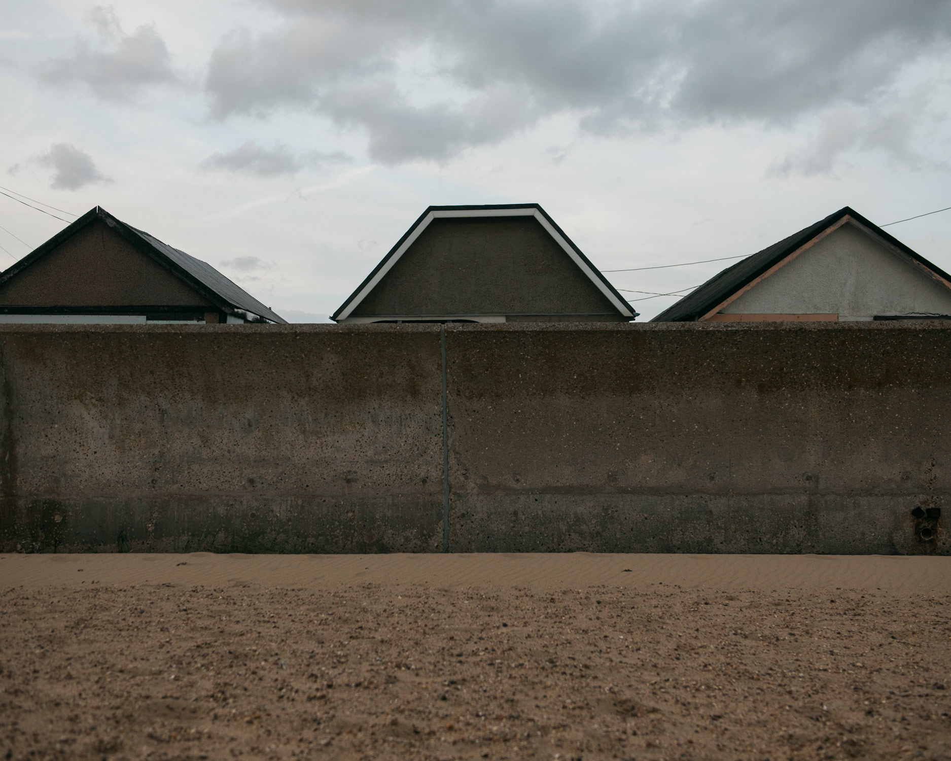 Jaywick's prefab houses are all only one storey high. The roofs comically appear to be peeking over the wall.