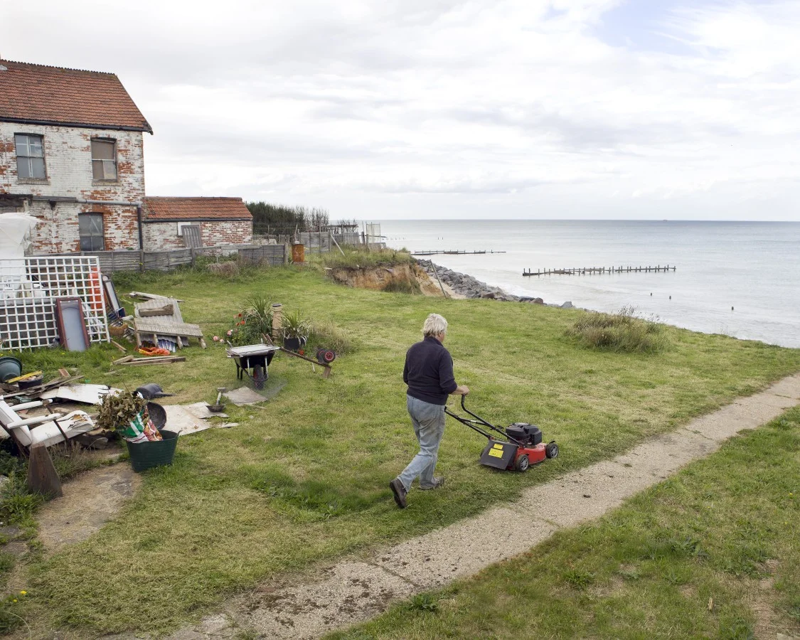 Happisburgh, Norfolk, is one of the hardest hit communities on the east coast. The government has relocated nearly all the residents from the sea front houses. In this picture Bryony Nierop-Reading, one of the only few remaining residents, mows the lawn of the bungalow she refuses to leave. "Why should I be made to move from the home I love? I think it would be totally immoral for me to take any money at all for it."