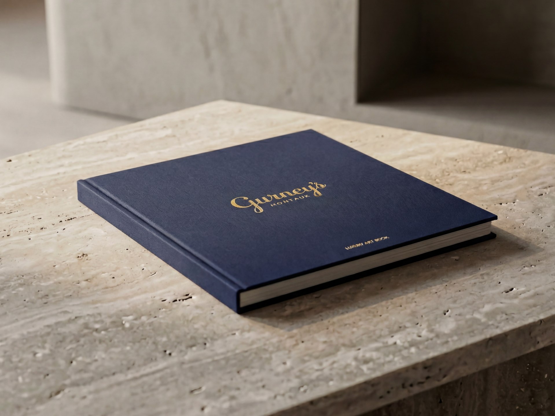 A navy blue hardcover book titled "Gurney's Montana" with gold lettering, resting on a beige marble countertop.