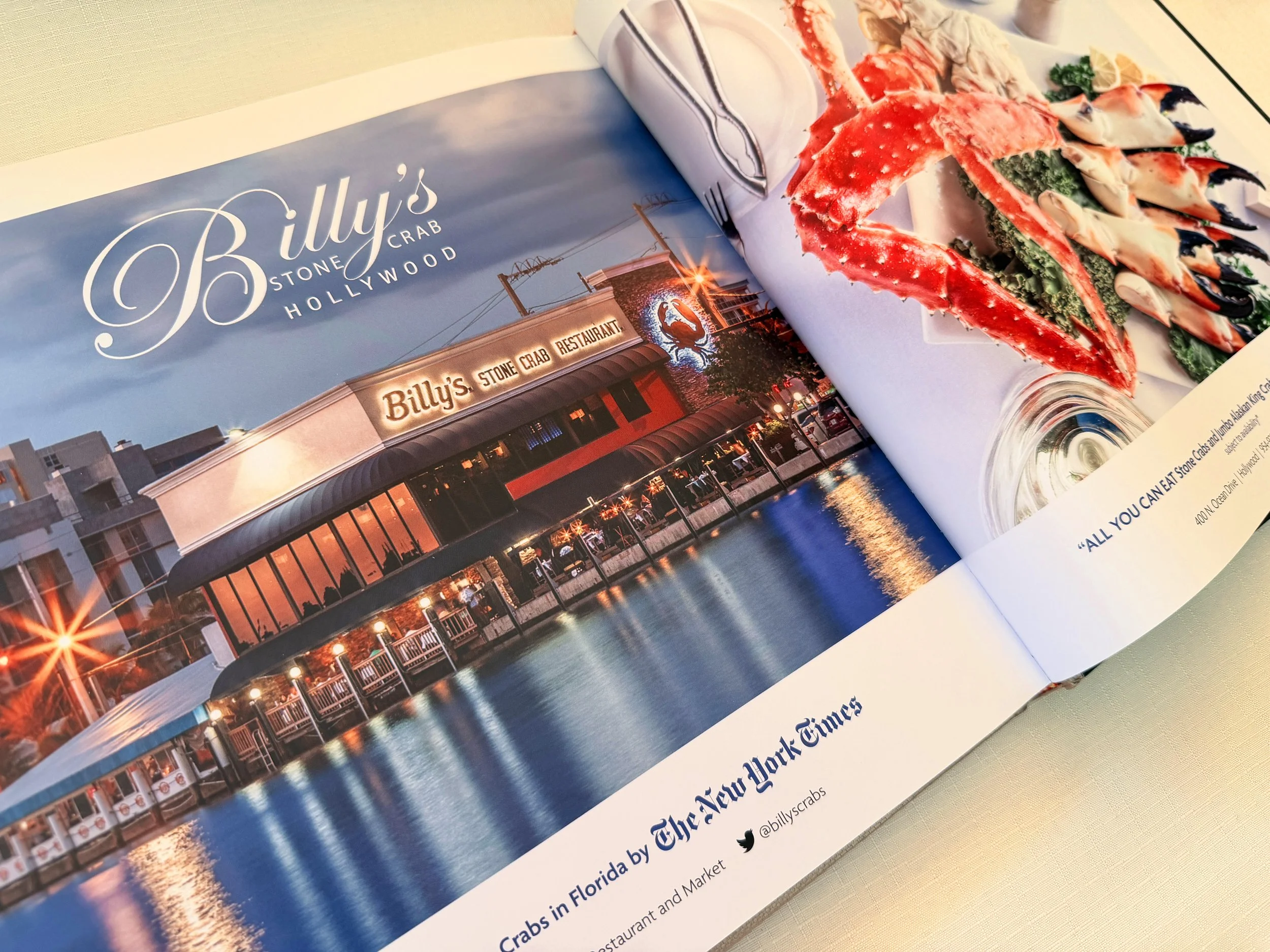 Open magazine featuring a photo of Billy's Stone Crab Restaurant in Hollywood, Florida, with a dish of king crab legs topped with a creamy sauce in the foreground.