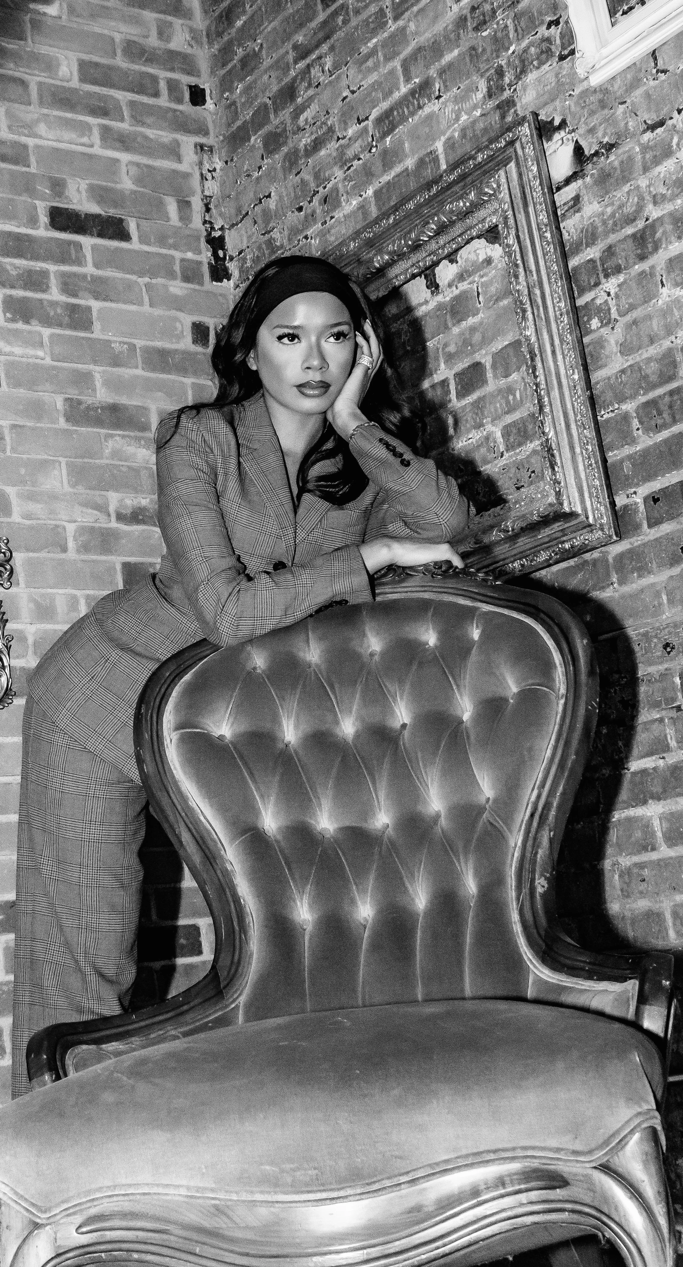 Creative hyphenate Kamika Bianca Guerra-Walker poses with confidence and appears contemplative but sure in Black and White photo with brick wall and detailed frame in the background