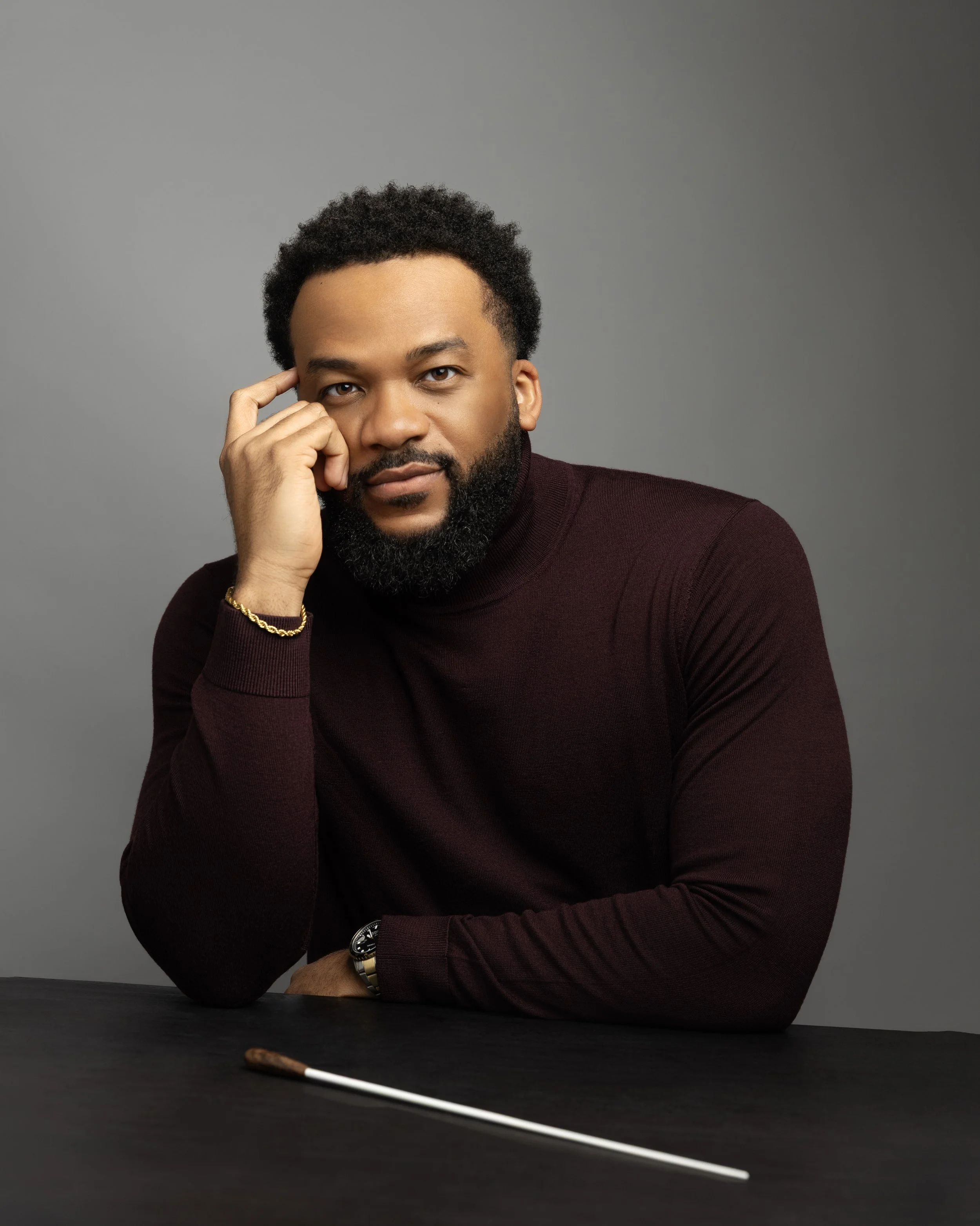 Composer and musical talent King Udofia poses in a professional headshot in brown turtle neck with gold chain and gold watch details