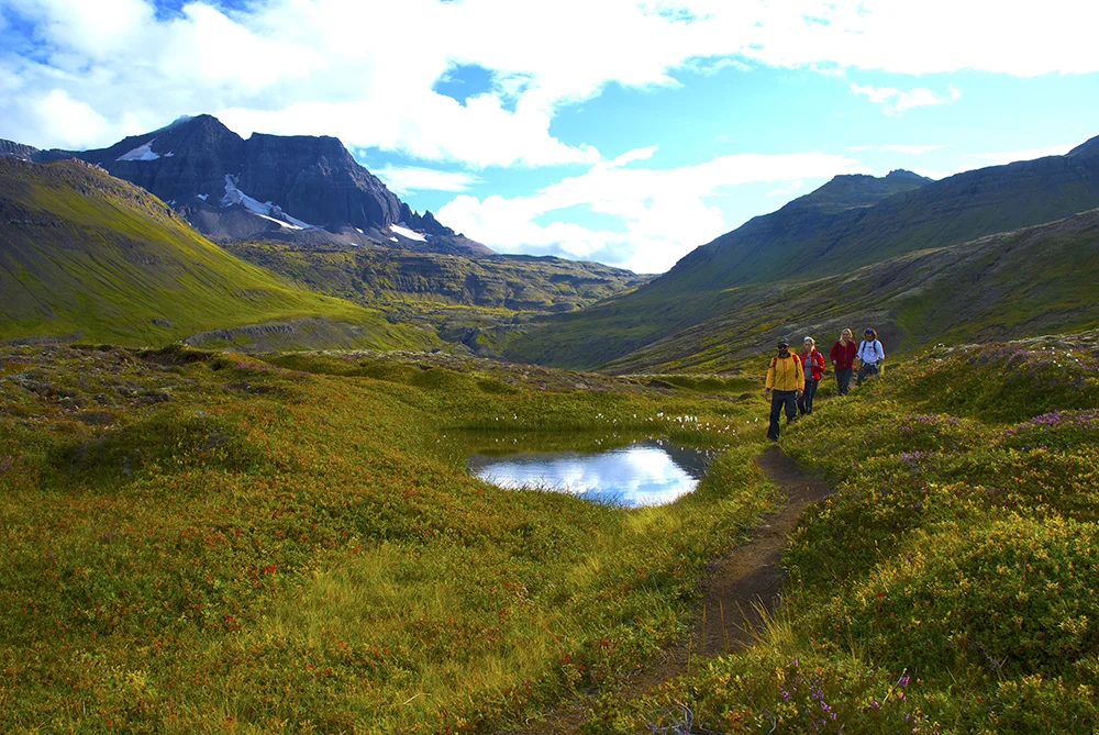 Group of hikers exploring trails by an alpine mountain lake during an Ashram spiritual retreat Iceland experience.