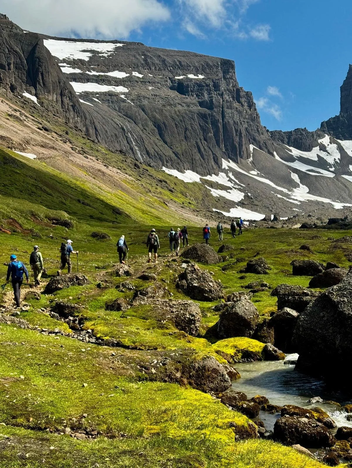 Group of Ashram hikers hiking in Iceland along an alpine stream in the foothills of dramatic glacier mountains