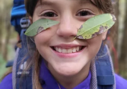 A smiling child outdoors with myrtle leaves stuck to their face
