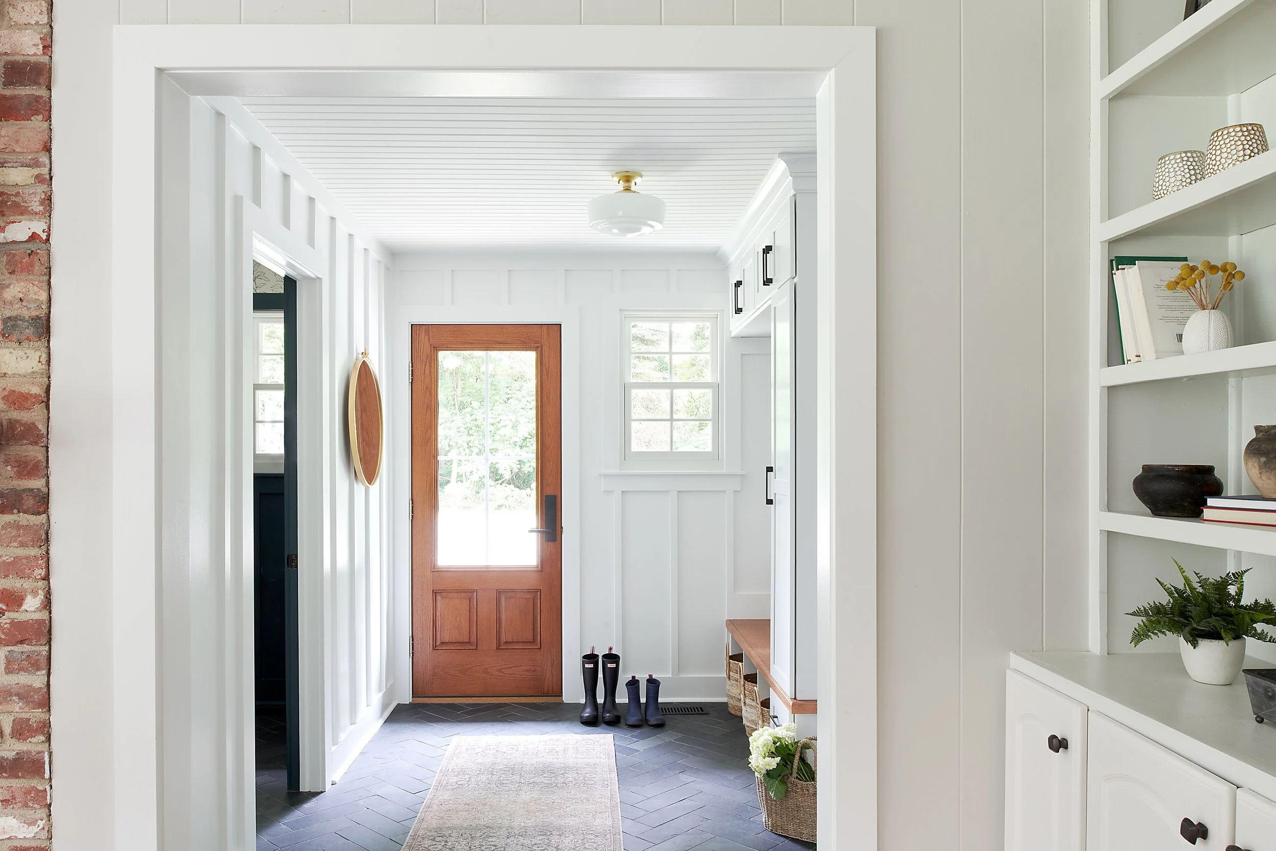Entry of a Rose Valley home renovation, custom white millwork, dark herringbone natural stone tile, brick wall, built in bookshelf.