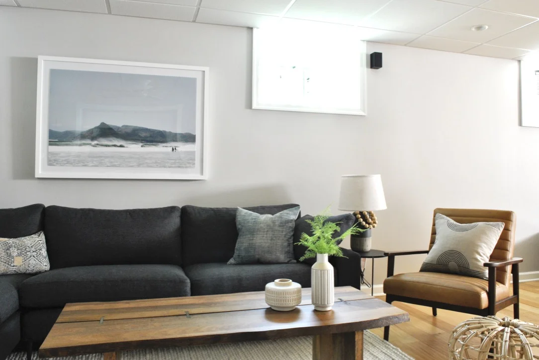 Basement family room complete with dark sofa and brown leather chair.