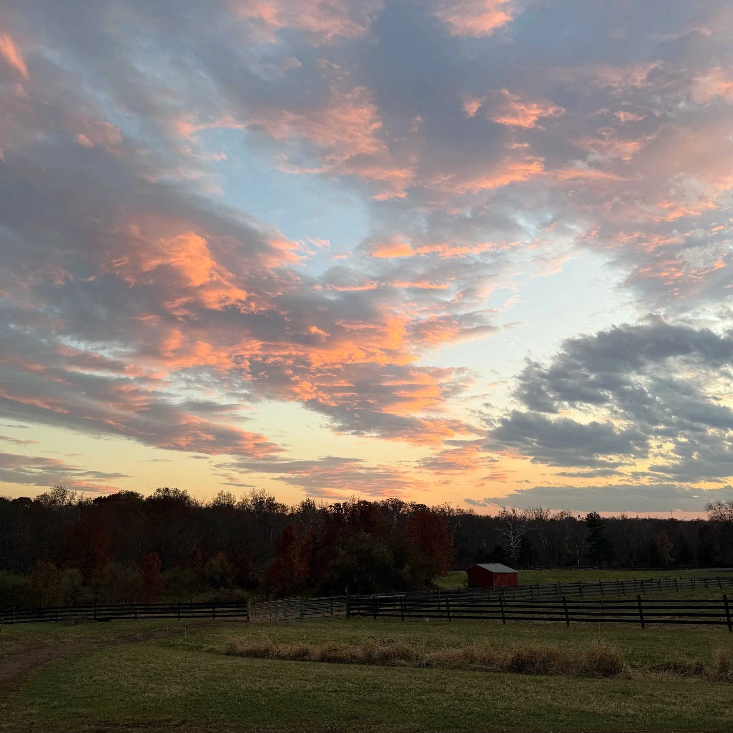 Sunset over a field with a fence and horse shed