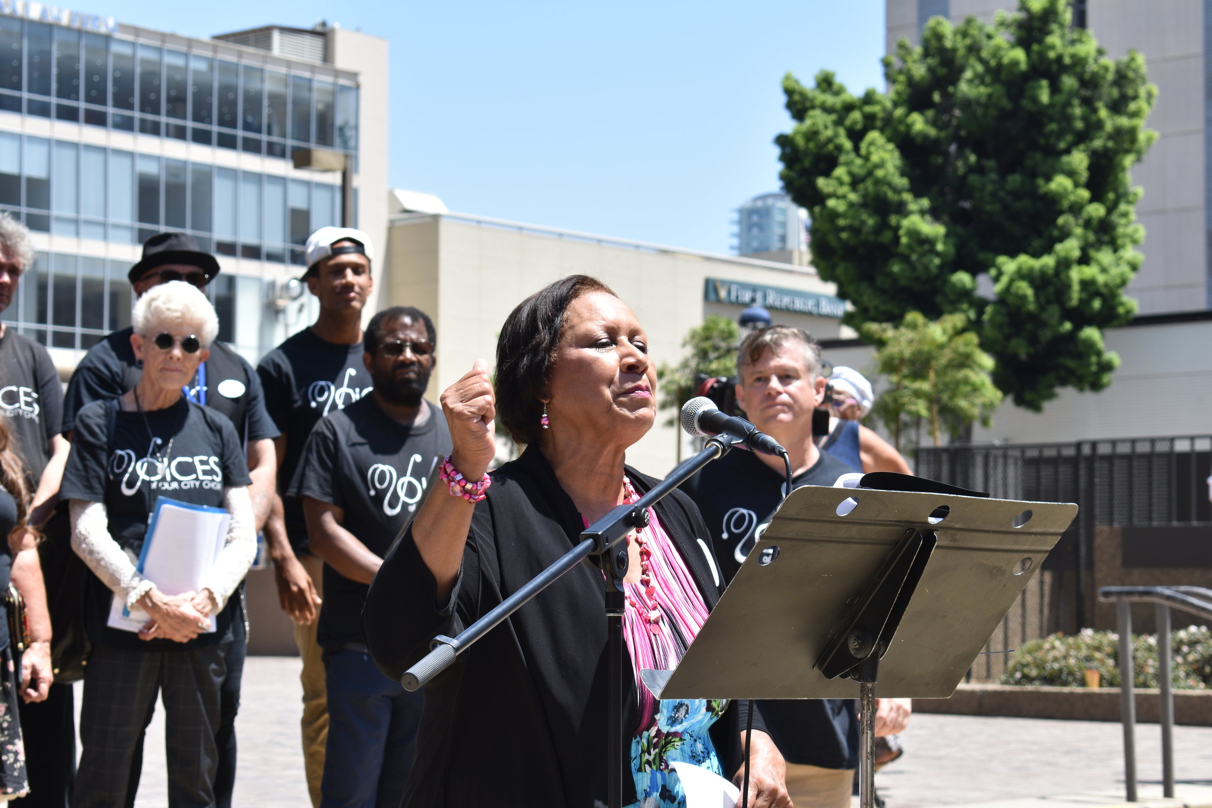 Jo Barrett, John Brady, and Voices of Our City Choir speaking before the rally, July 2019