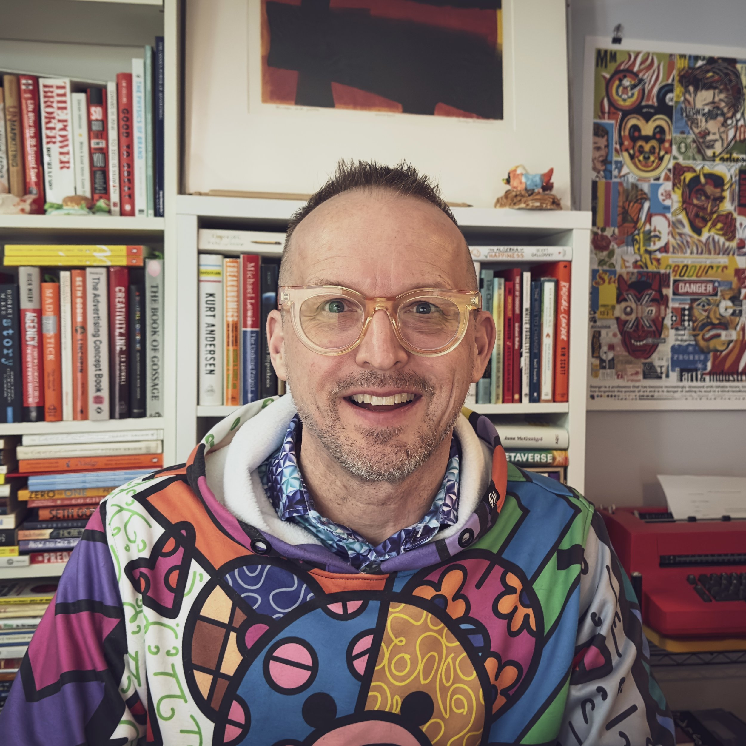 Portrait of Tim Brunelle in his home office, in front of a bookshelf and IBM Selectric typewriter.