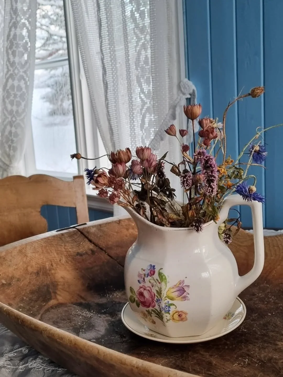 Blomstene er fra sensommeren i fjor, t&oslash;rkede, frosne.
P&aring; vindusglassene strekker isrosene seg utover.
Utenfor er det hvit sn&oslash; overalt.
Men det ER noe i lufta.
Et streif av et annet lys, et hviskende h&aring;p om skifte i temperatu