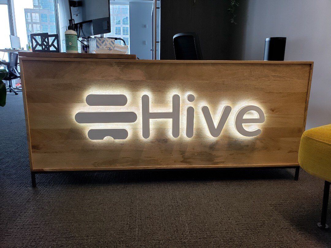 backlit / halo-lit fabricated dimensional individual 1.00&quot; thick deep painted white stainless steel metal logo/letters, pin-mounted onto face of wood desk floating off 1.00&quot; and illuminated with White LEDs from behind. #interiors #officeint