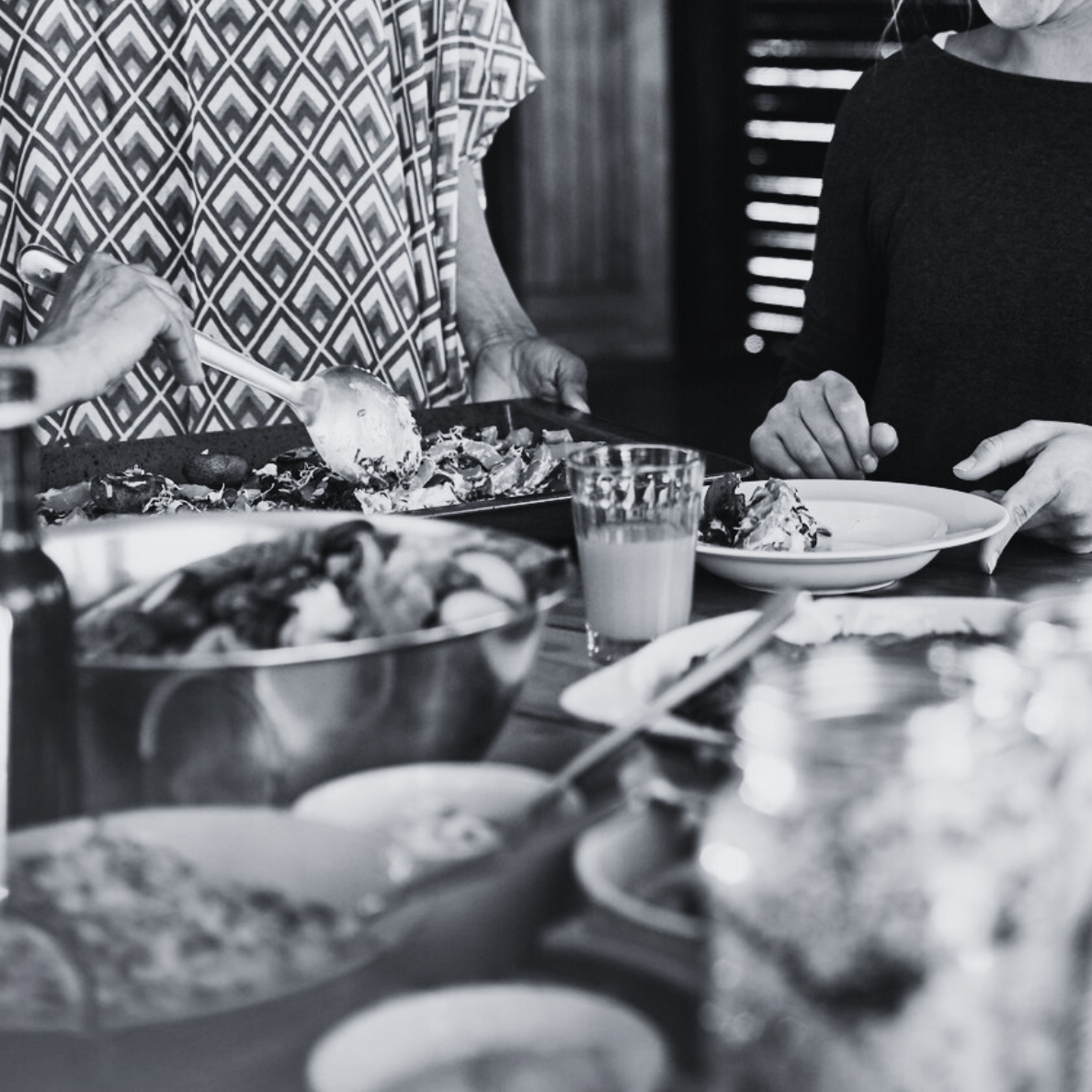 People serving themselves food at a buffet table with various dishes, including salads and drinks, in a casual dining setting.