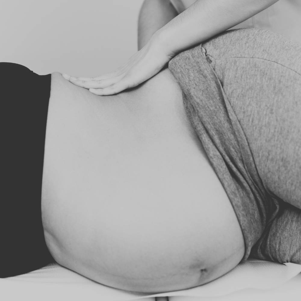 A person receiving a medical massage or physical therapy on their abdomen, with the therapist placing hands on the person's stomach.