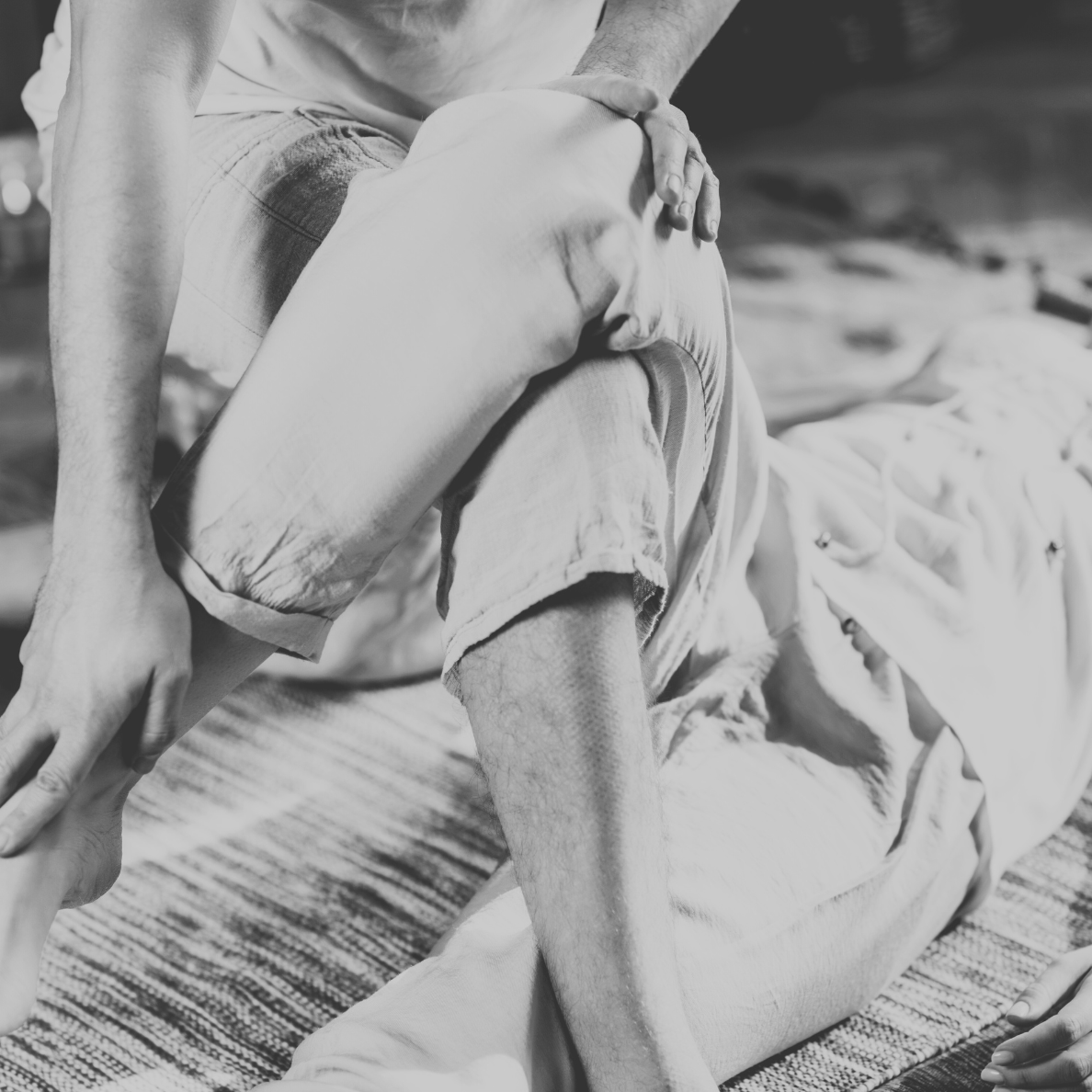 A person receiving a massage, lying face down on a mat, with another person applying pressure to their shoulder.