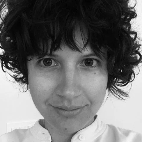 A black and white close-up portrait of a woman with short, curly hair smiling at the camera.