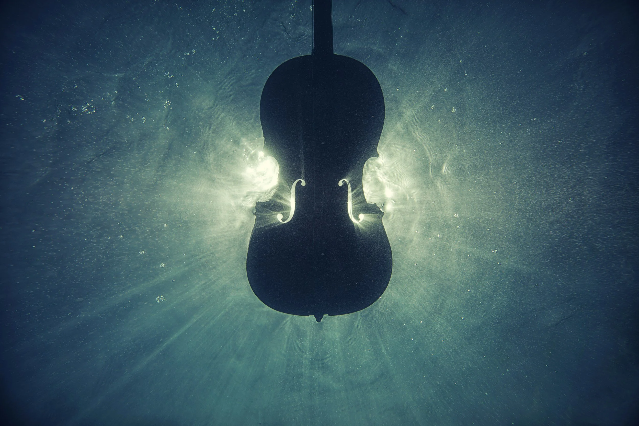 A violin submerged underwater with sunlight filtering through, creating a glowing effect around it.