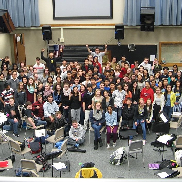 Group photo of students and teachers in a classroom, some students are standing and some are sitting, with a blackboard and educational equipment in the background.